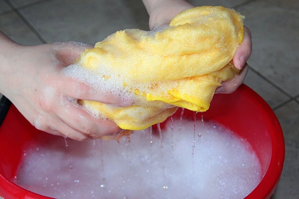 A person off-screen squeezing soapy water out of a rag