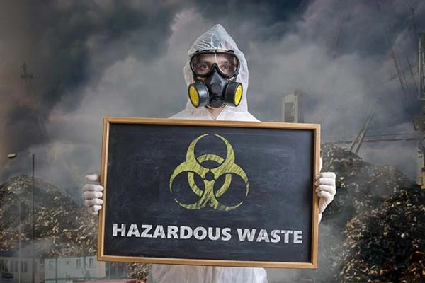 A-man-in-protective-gear-holding-a-hazardous-waste-sign