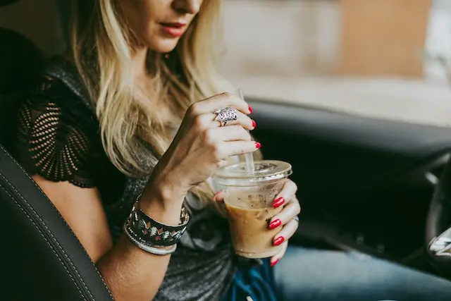 A woman sitting in a car and drinking iced coffee