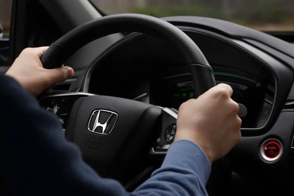 A person sitting in a Honda and holding the steering wheel