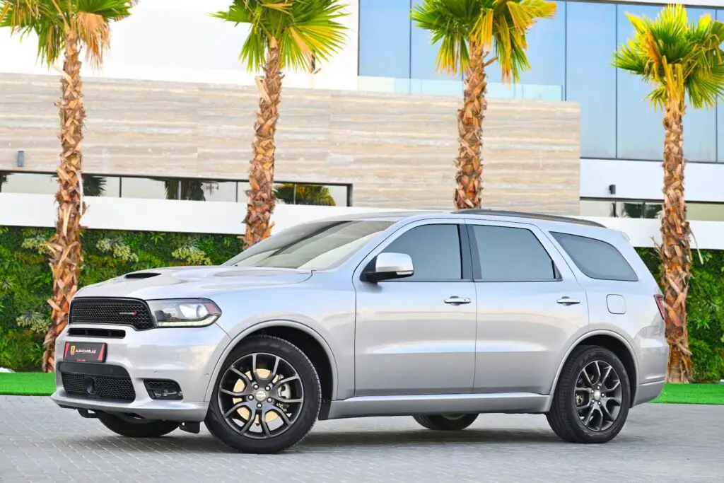 A silver Dodge parked in front of palm trees