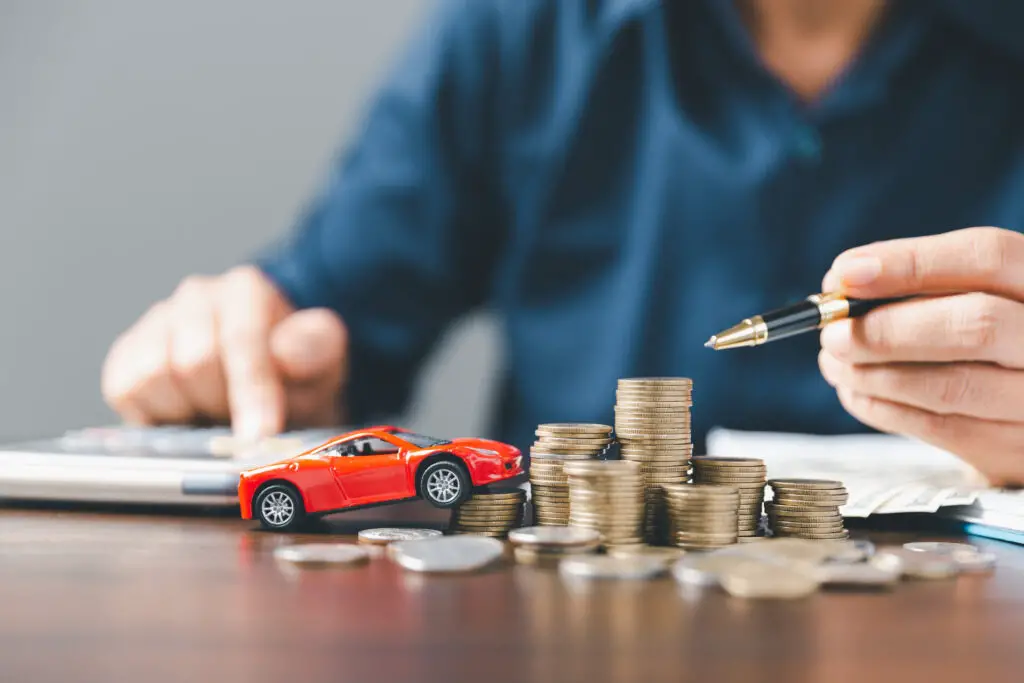 Person counting expenses with a red toy car and a stack of coins