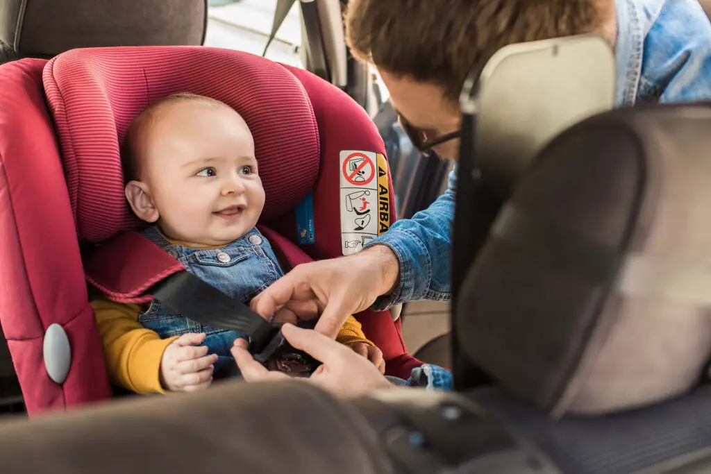 Father fasten his little baby in the car seat