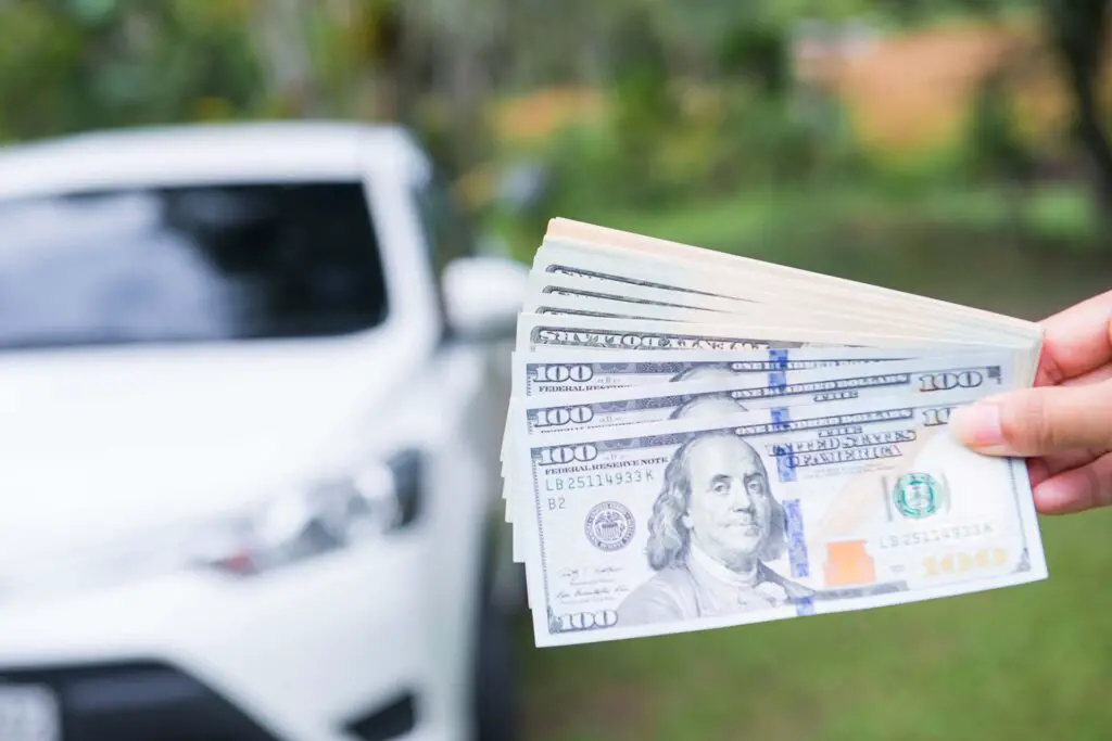 Person holding money in front of a car