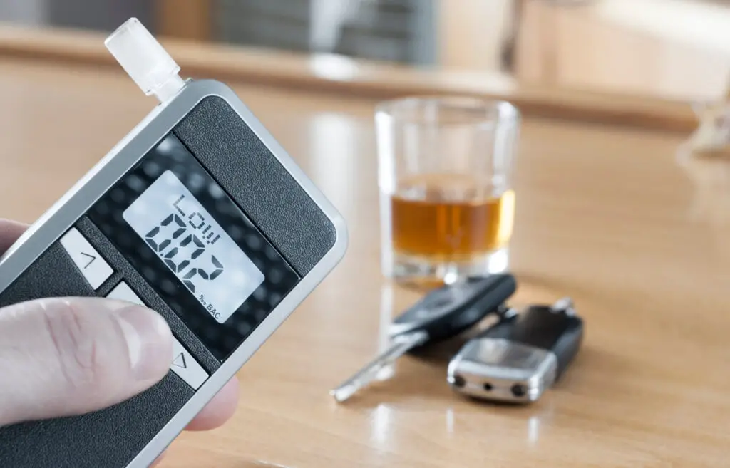 A breathalyzer showing 0.02 with beer and car keys in the back