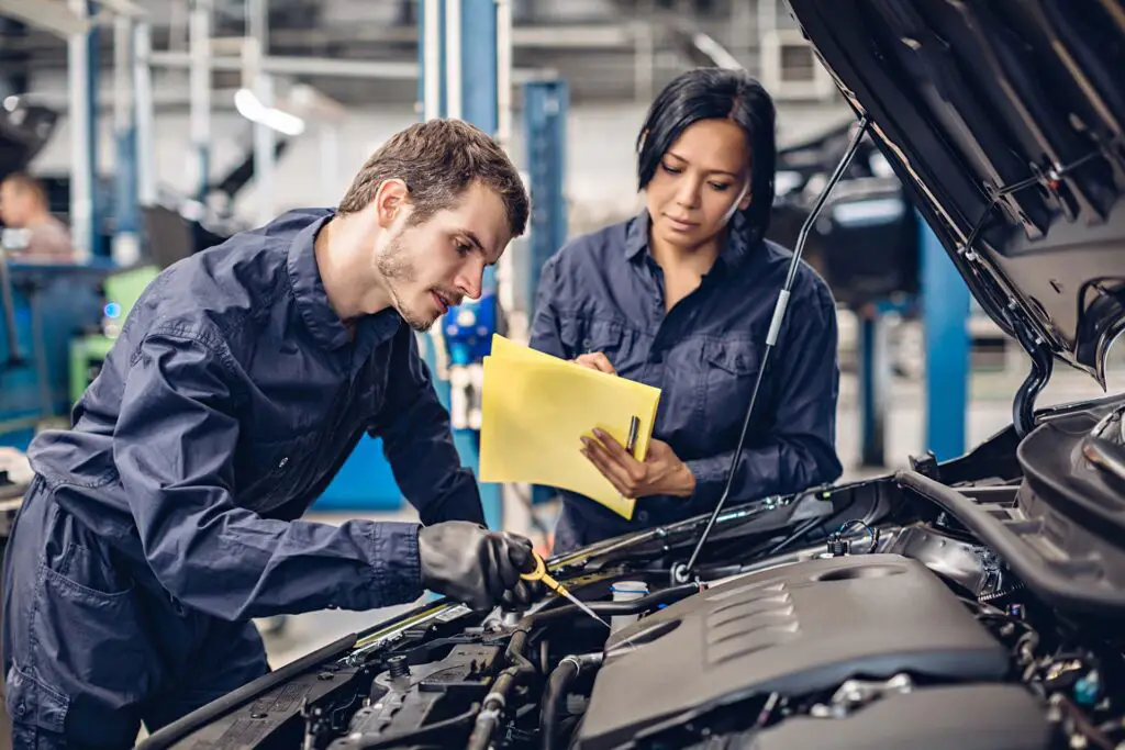 Auto car repair service center. Two mechanics - man and woman examining car engine