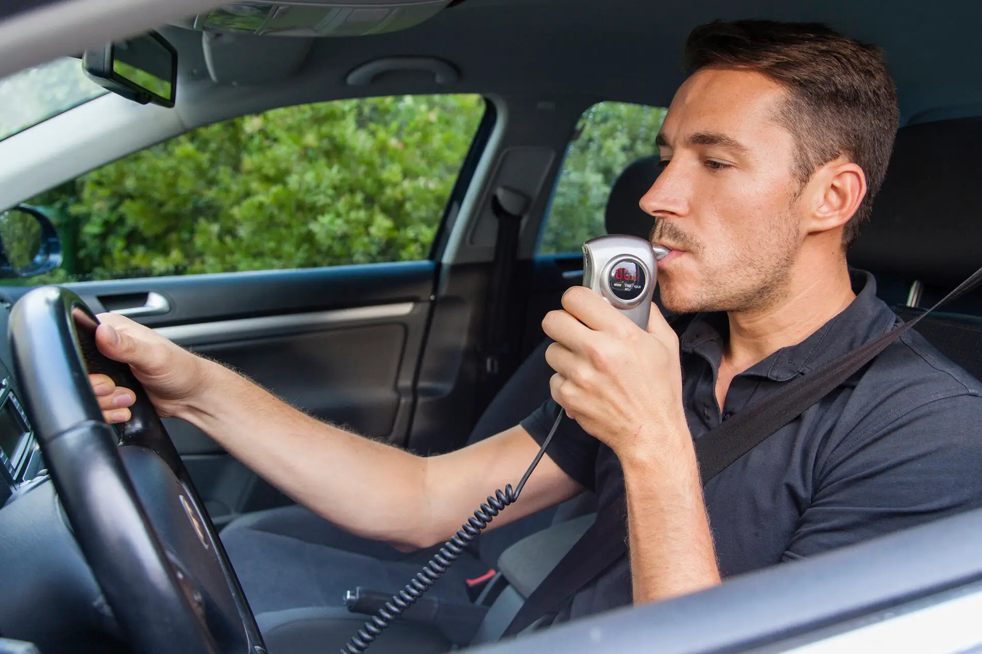 A man blowing into a breathalyzer while sitting behind the wheel
