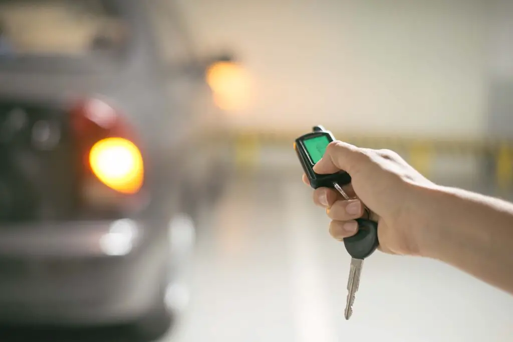 hand presses on the remote control car alarm systems at underground parking with car on background