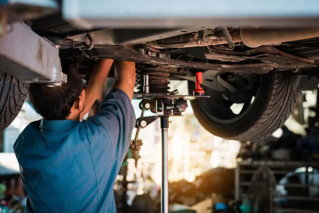 Mechanic repairing a car, Mechanic inspects car suspension system and chassis with a torch-lite under the car.