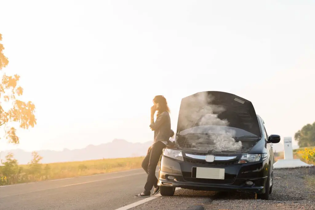 Broken car. Lady standing on the road by the broken car in the middle of nowhere. Making telephone call to get help with the broken car. smoke coming out the engine. Help needed. Car service. Tow service.