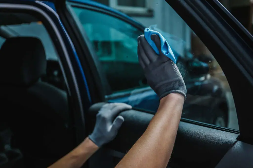 Worker cleaning car window after applying tinting foil