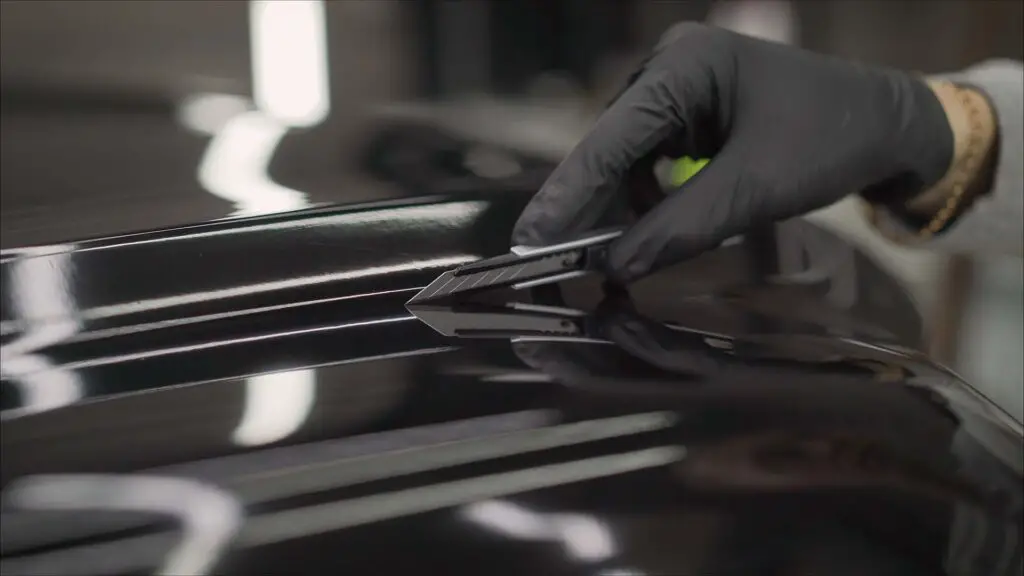 The protective film is removed from the machine with a paper knife. Car wrapping specialists straightening vinyl foil or film to remove ari bubbles cut carbon film