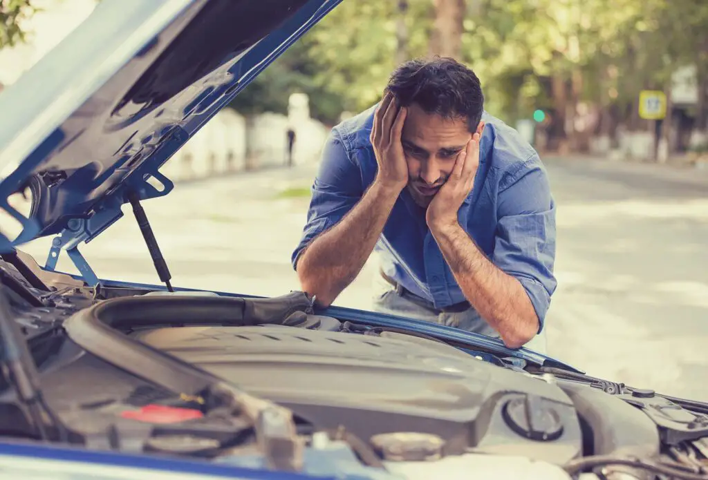 young stressed man having trouble with his broken car looking in frustration at failed engine