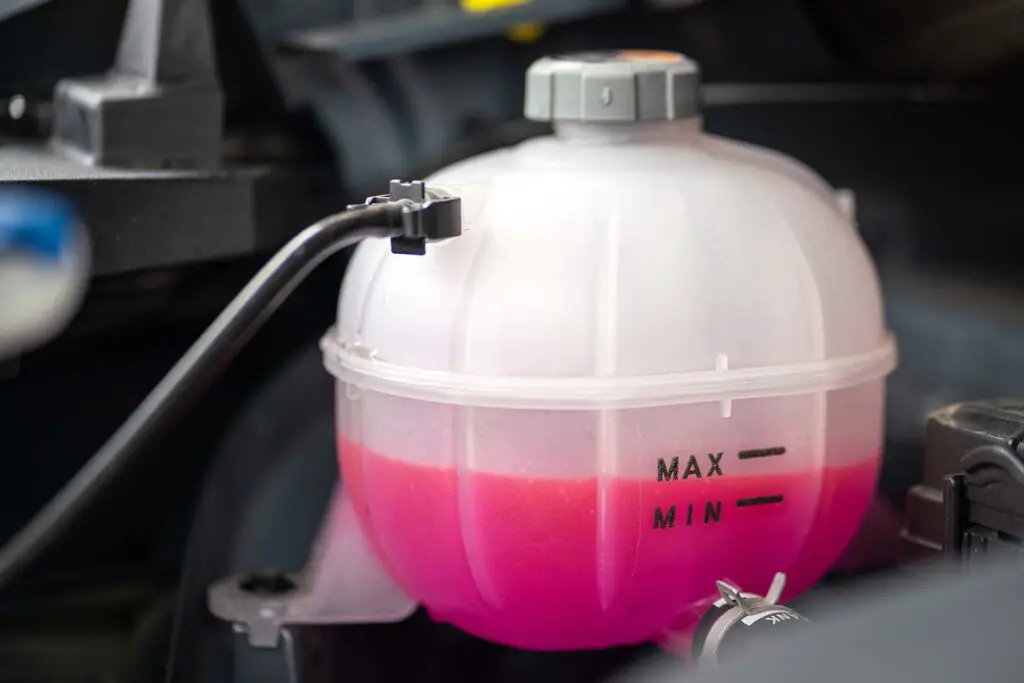 A car's engine coolant water supply box filled with pink color antifreeze liquid