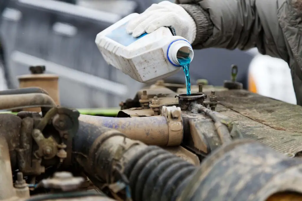 An auto mechanic pours antifreeze into the radiator of an old car engine.