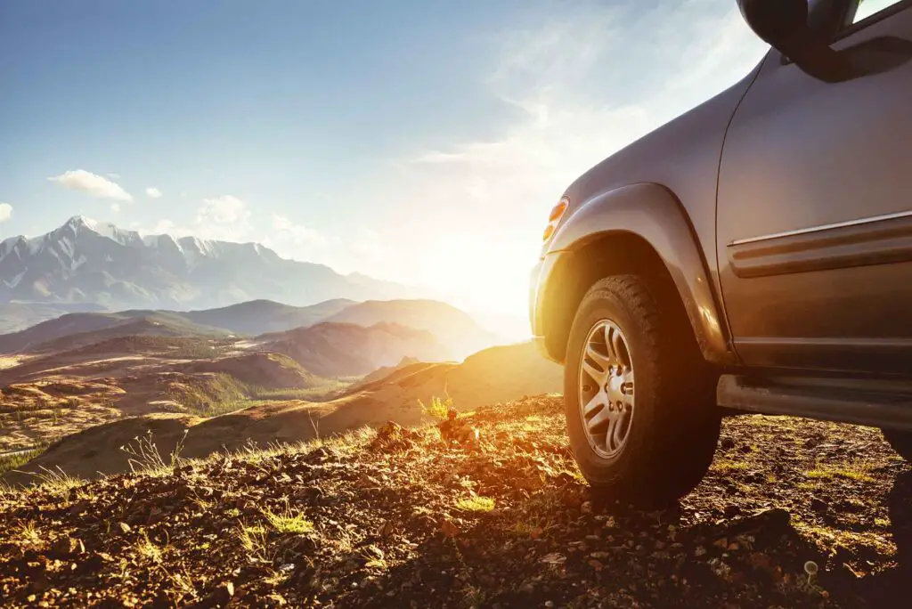 Travel concept with big 4x4 car against sunset and mountains. Closeup photo of off-road wheel