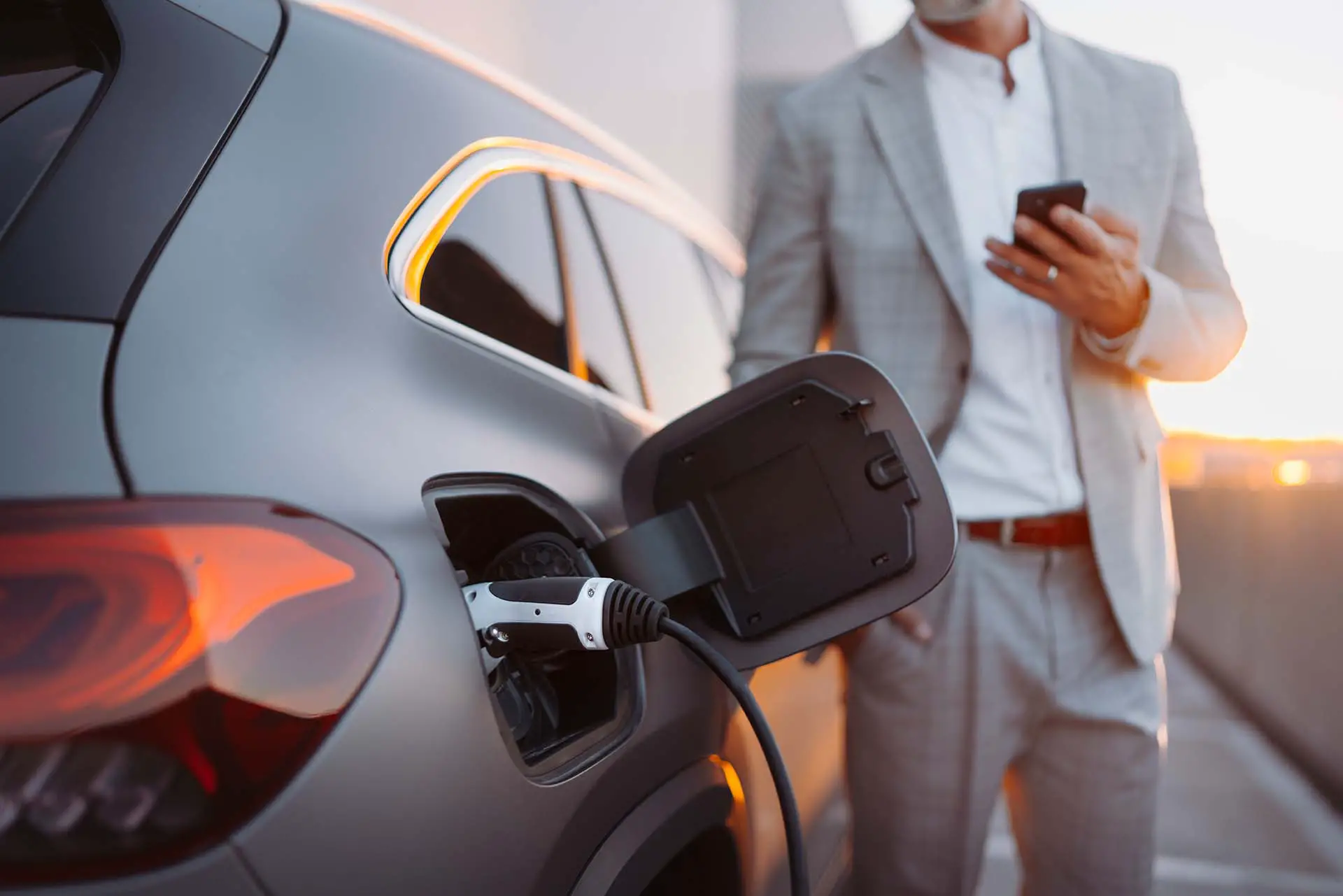 A man holding smartphone while charging car at electric vehicle charging station, closeup.
