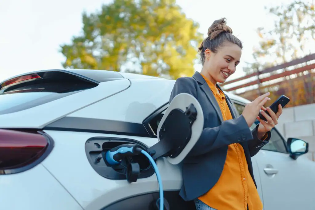 Young woman with smartphone waiting while her electric car is charging
