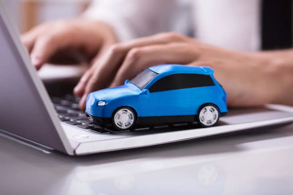 Person typing on a laptop with a blue toy car on the keypad