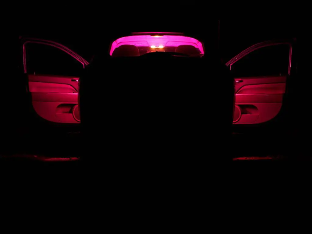 car with a red light inside on a dark night. open doors. back view.