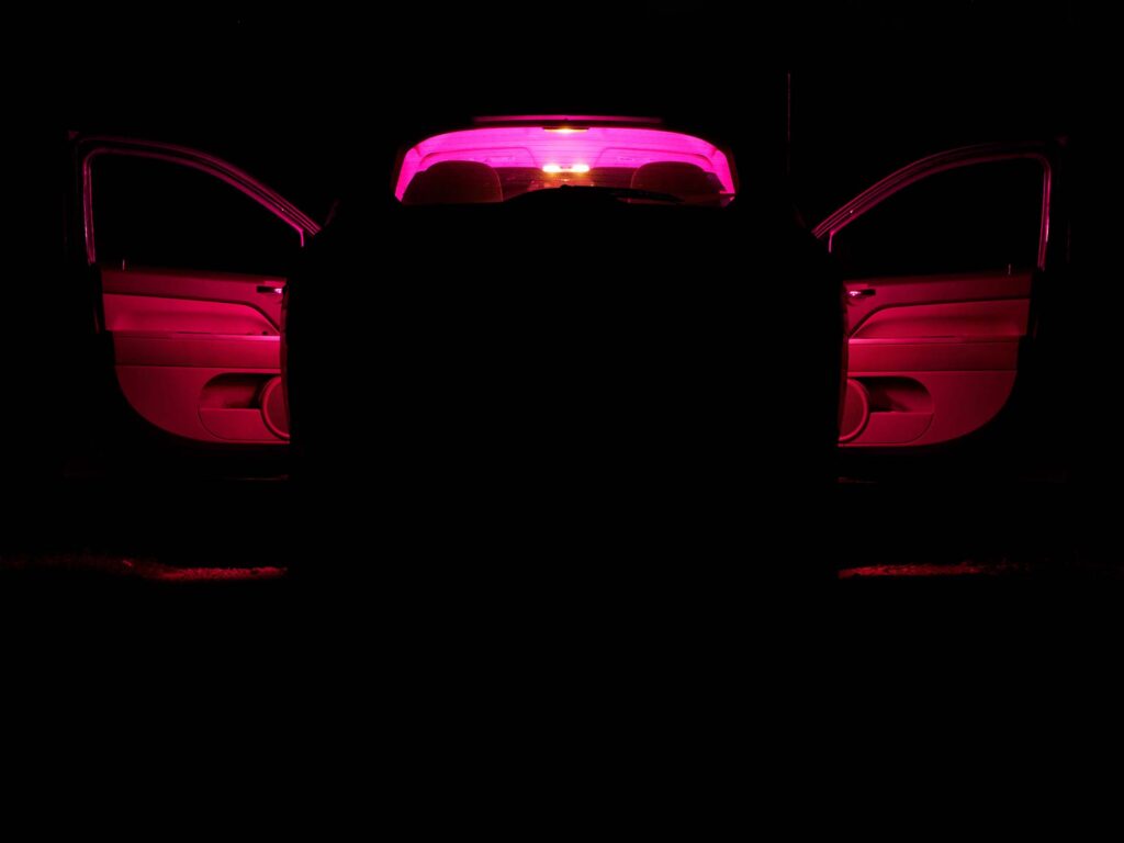 car with a red light inside on a dark night. open doors. back view.