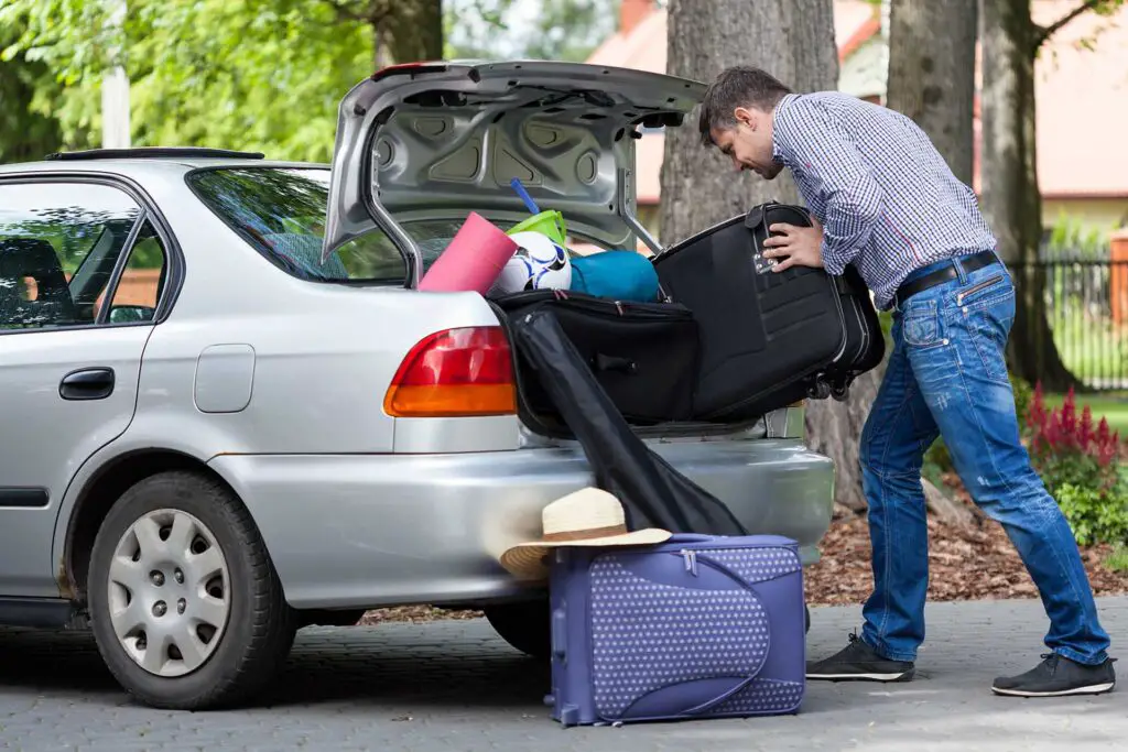 Horizontal view of a man trying to putting a travel bags into a car