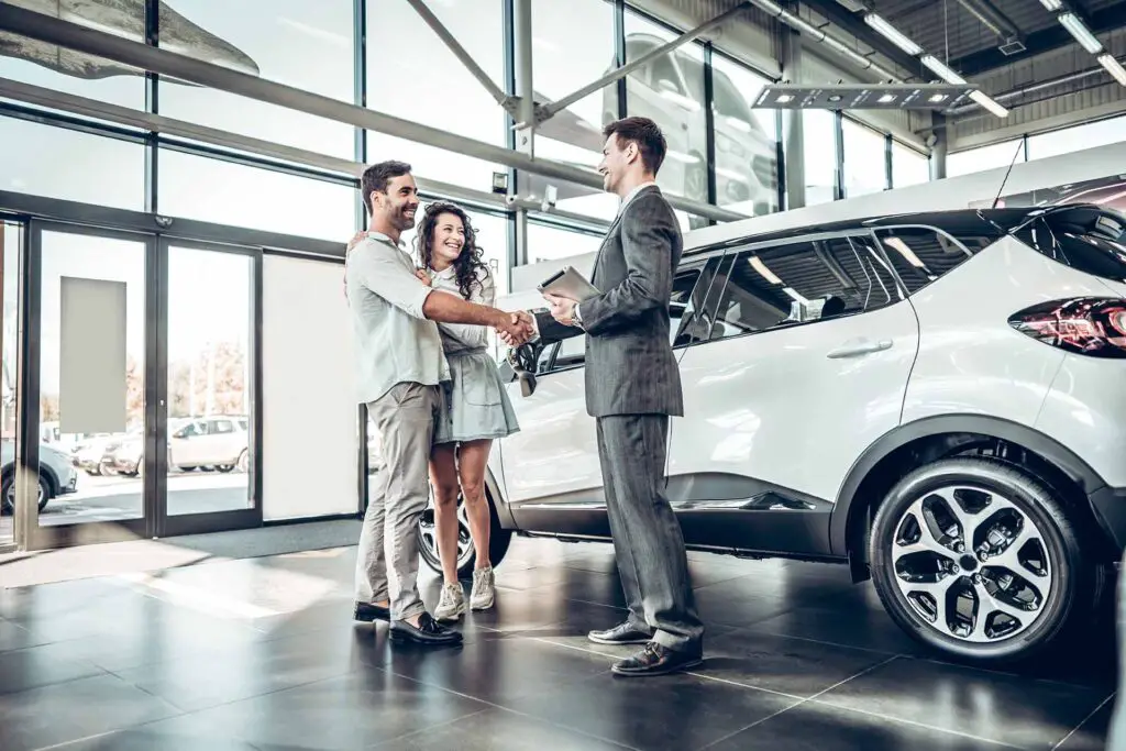 Young couple shaking hands with sales agent after a successful car buying.