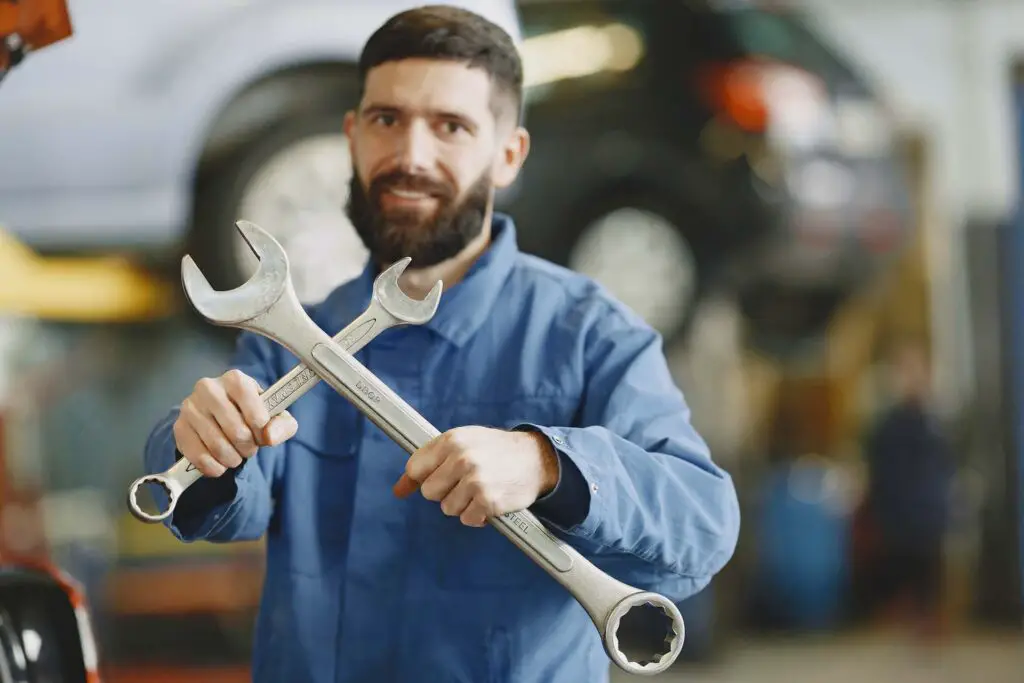 A mechanic in a car shop holding two big wrenches