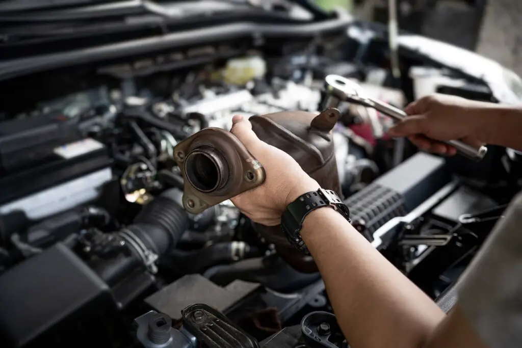 Close up old catalytic converter in hand Car service man and holding a wrench for remove part in engine room of car , service and maintenance concept in garage