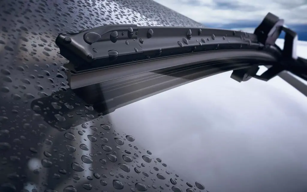 A closeup of a car windshield with raindrops and a frameless wiper blade