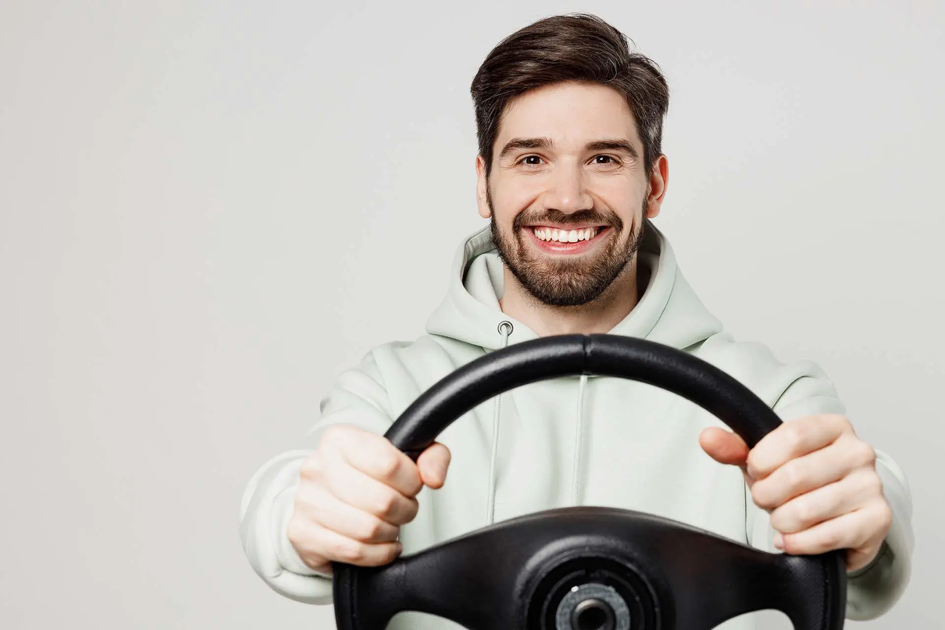 Young smiling happy fun satisfied cheerful man wear mint hoody hold steering wheel driving car