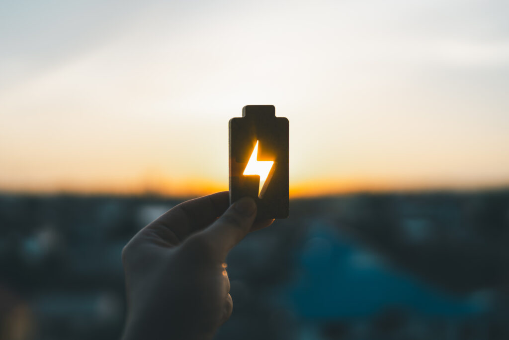 Person holding an electric battery symbol at sunset