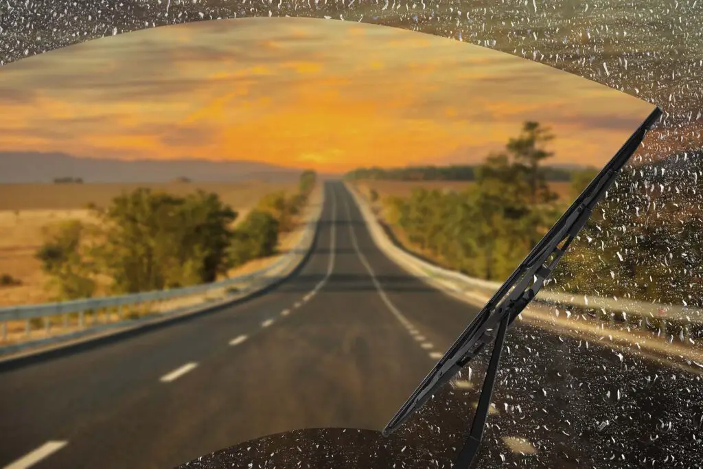 Car windshield wiper cleaning water drops from glass while driving