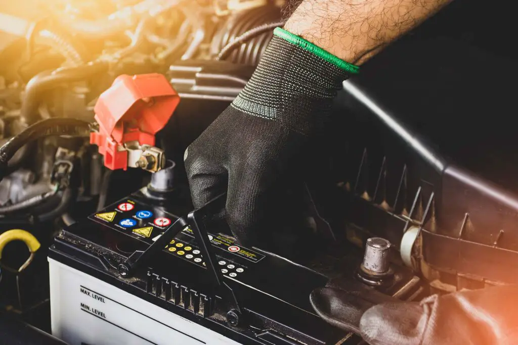 The Mechanic's hand is pulling up a car's old battery for replacement
