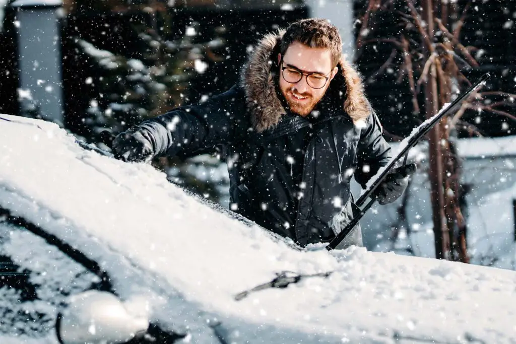 A man cleaning his car covered with snow