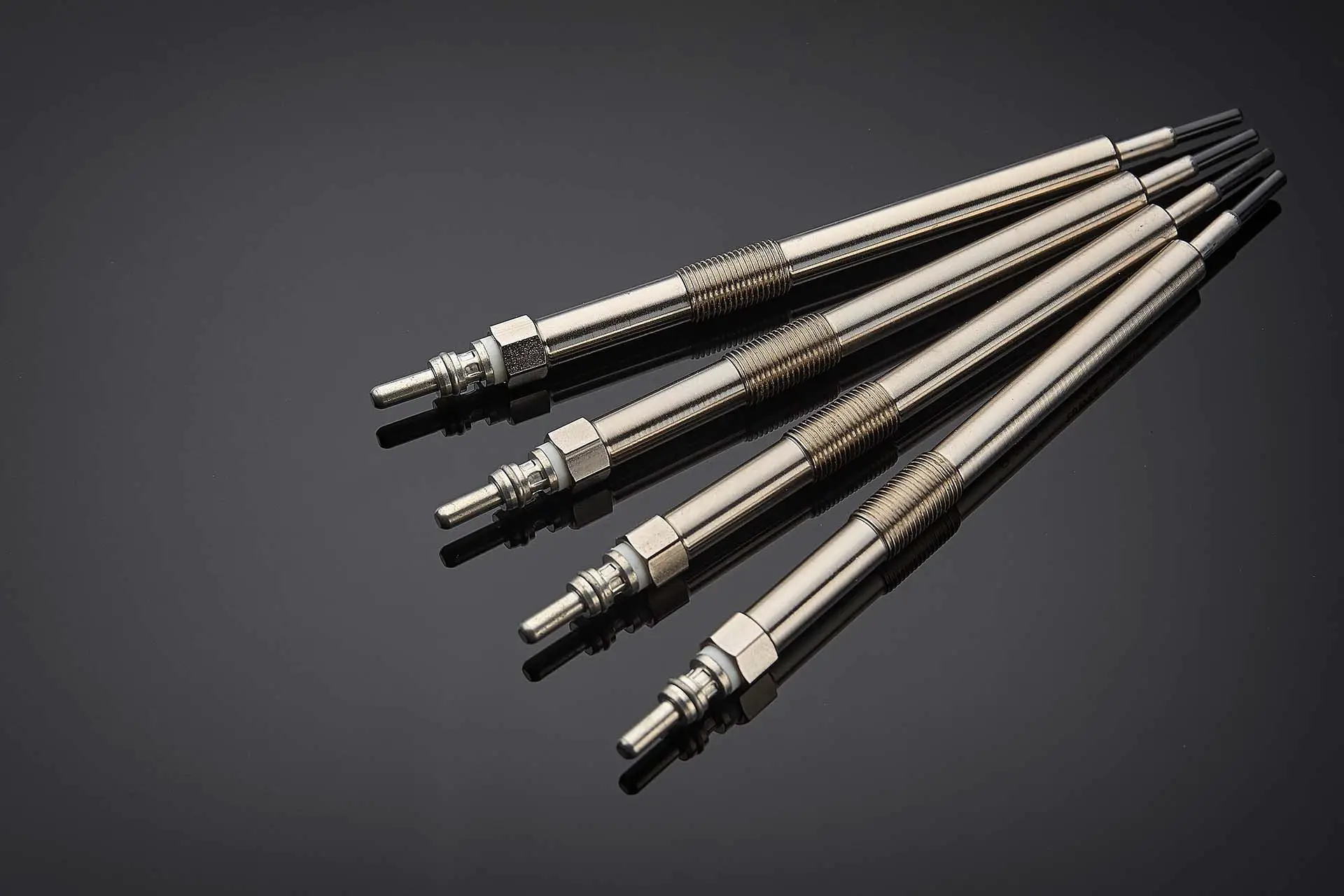 Four glow plugs for the diesel engine lie on a dark background, prepared for the next service