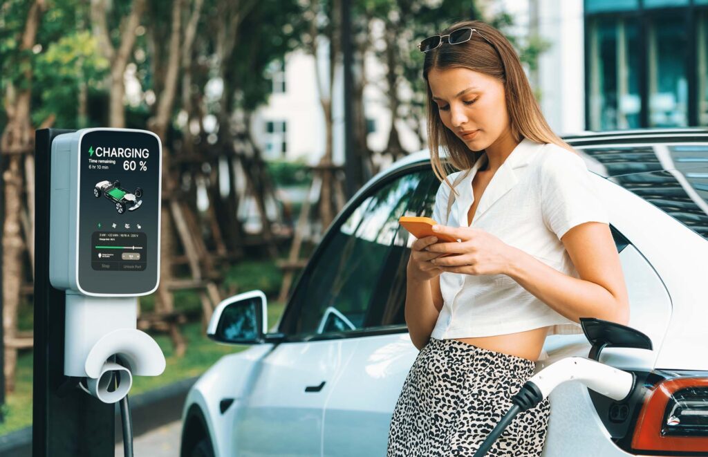 Young woman travel with EV electric car charging in green sustainable city outdoor garden in summer. Urban sustainability lifestyle by green clean rechargeable energy of electric BEV vehicle innards