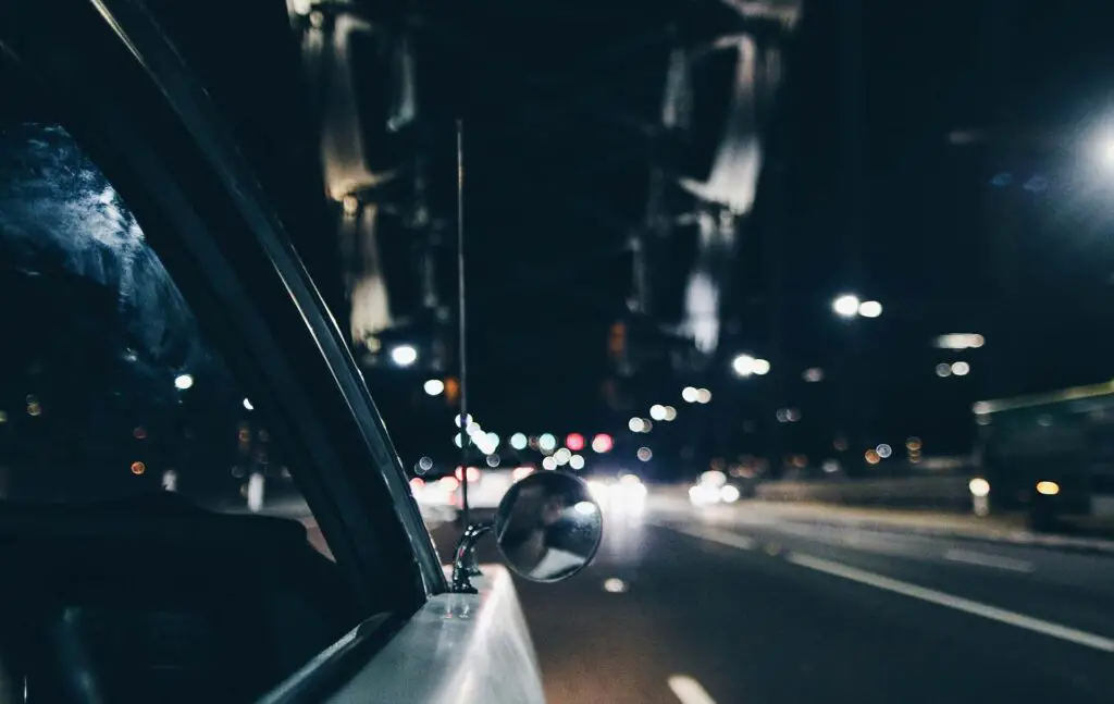 An antenna and a side mirror on a car during the night