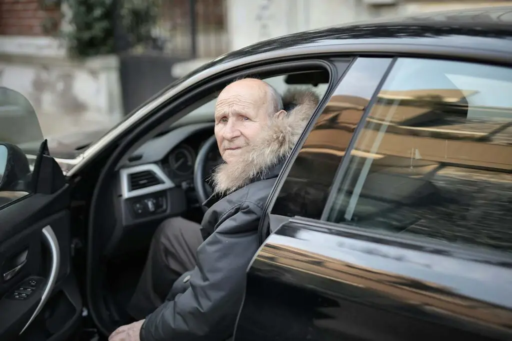 An older man in a black leather jacket entering his car