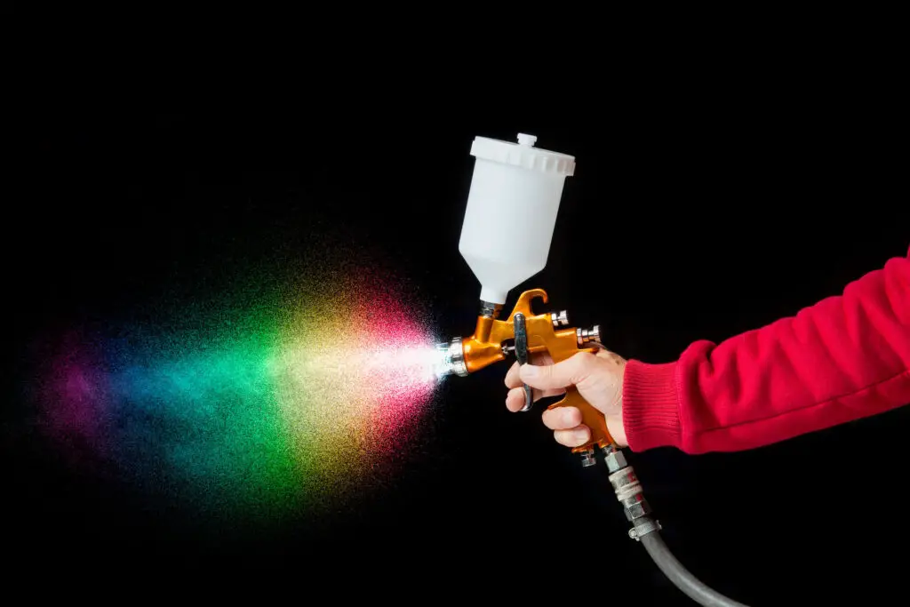 A person holding a paint sprayer against a black background 