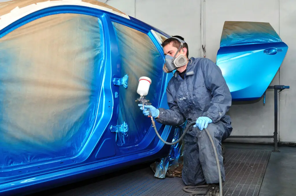 A professional car painter painting a car in blue 