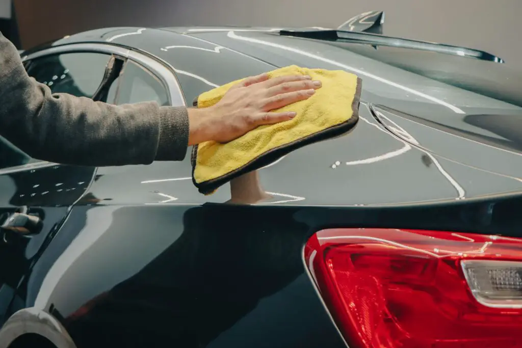 A hand with a cloth cleaning a car