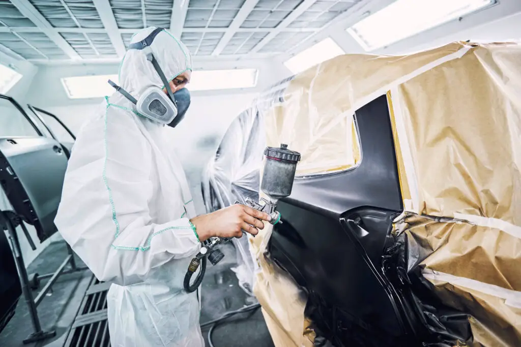 A man in protective gear spraying a car with matte black paint 